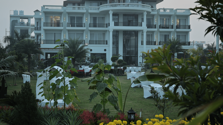 Front view of a white multi-story luxury hotel with balconies and white wicker seating on a large green lawn.