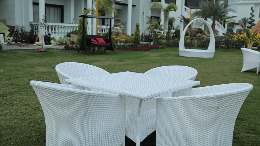 A white wicker dining set on the green lawn with the resort's white balcony suites in the background.