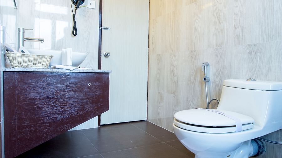 A bathroom at New Orchid Lords Inn Gangtok contains a toilet, a sink with a mirror, a door, and a folded towel on the floor.