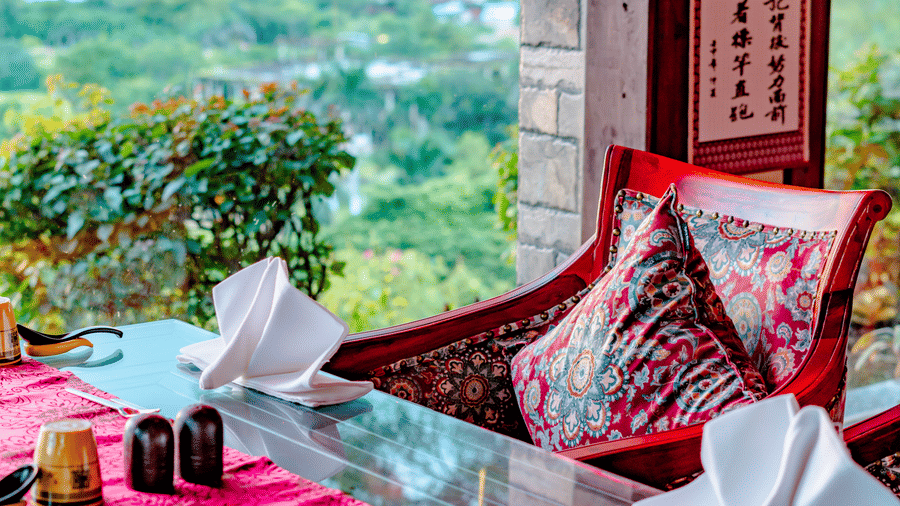 An elegantly set table at Ming Dynasty, found at Noor-Us-Sabah Palace, Bhopal, featuring red runners and traditional decor with a stunning view of the surrounding greenery.