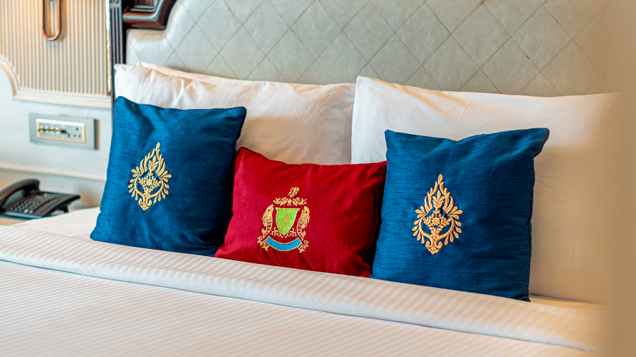 Close up of a plush double bed with blue and red-coloured cushions in the Royal Club Room at Noor-Us-Sabah Palace, Bhopal.
