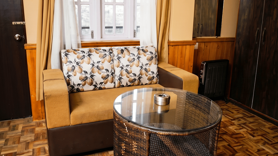 A cosy sitting area with parquet flooring, a tan sofa, and a unique dark wood barrel-style coffee table. 