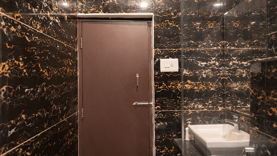 A washroom with a door at the corner and a sink and toilet on the side at Parampara Resort & Spa, Kushalnagar.