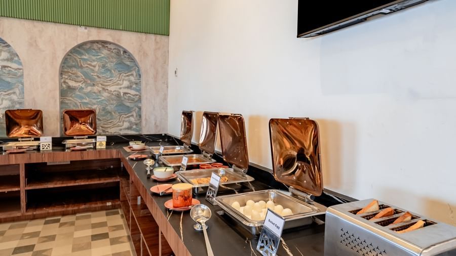 Close-up of a buffet station with juices, fruits, and pastries | Pravasa Hotel, Vijayapura