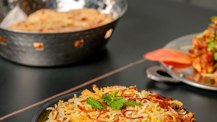 Bowl of biryani or pulao on a black table next to a small dish | Pravasa Hotel, Vijayapura