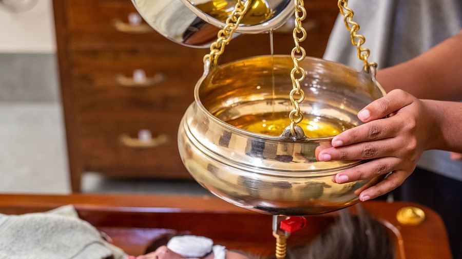 An image if a person transferring massage oil from one container to another which will be used for massage on a woman laying below it - Rajbagh Wellness