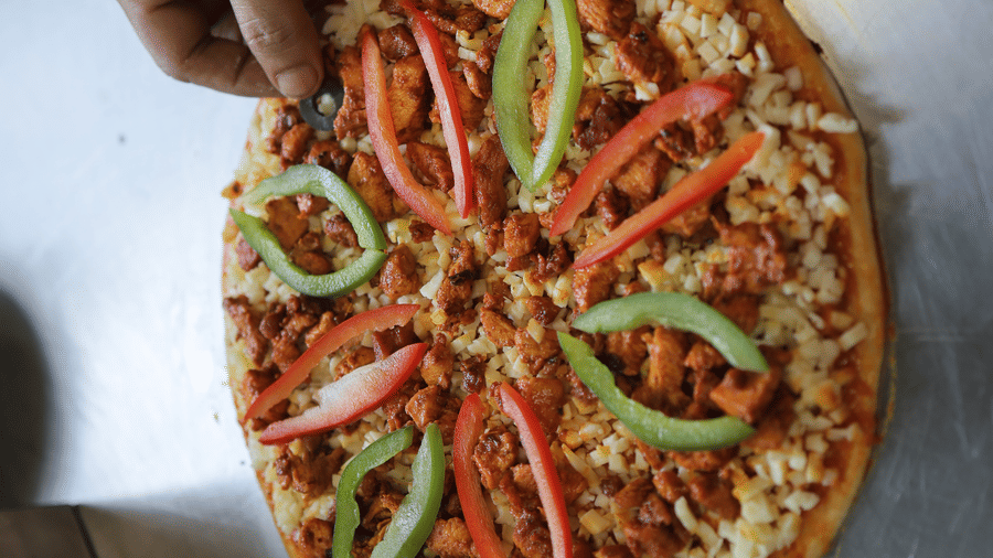 A hand placing a freshly cooked pizza topped with green peppers on a metal kitchen counter.