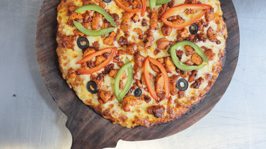 A freshly baked pizza with colourful toppings served on a circular wooden paddle board.