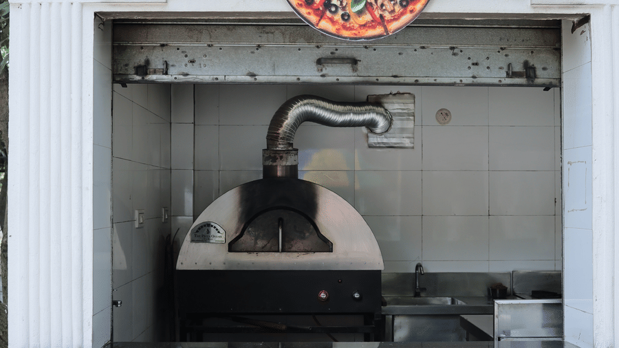 A white, outdoor wood-fired pizza oven built into a wall, decorated with a colourful pizza emblem.
