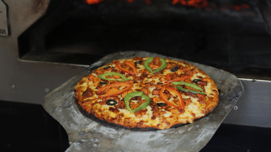 A pizza on a metal peel being slid into a hot, glowing wood-fired stone oven.