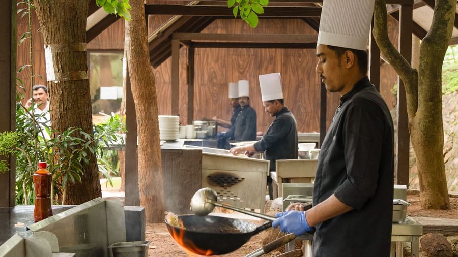 A chef in a white uniform prepares food at a buffet station in a dining area surrounded by lush greenery and large windows | Lake View Restaurant
