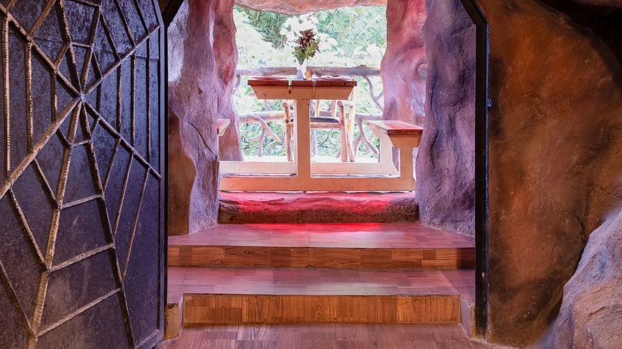 A narrow, arched entryway with reddish-brown tiled floors leads into a dimly lit, cave-like interior with a distant fountain | Cave Restaurant