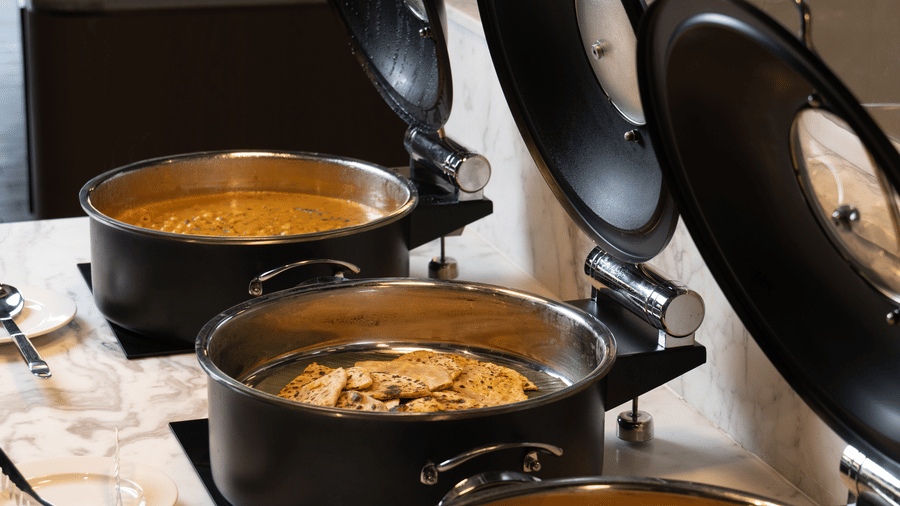 A row of 3 black ceramic cooking pots with open lids on a white marble buffet at Sands Point Hotel, Pondicherry.