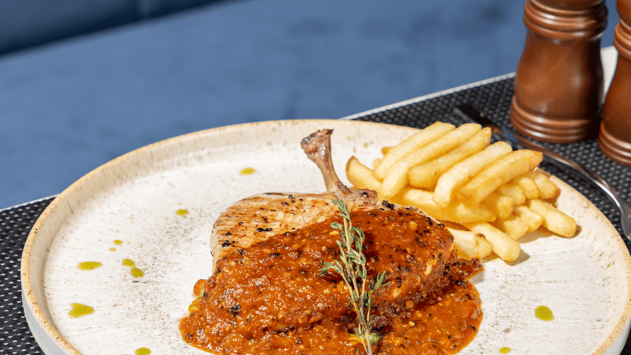 Close-up of a seasoned cut of meat served with fries and a garnish of fresh herbs at Sands Point Hotel, Pondicherry.