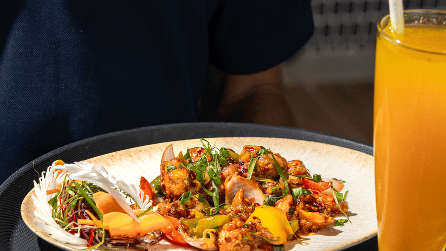 A staff member carrying 1 plate of stir-fried vegetables and a glass of orange juice at Sands Point Hotel, Pondicherry.