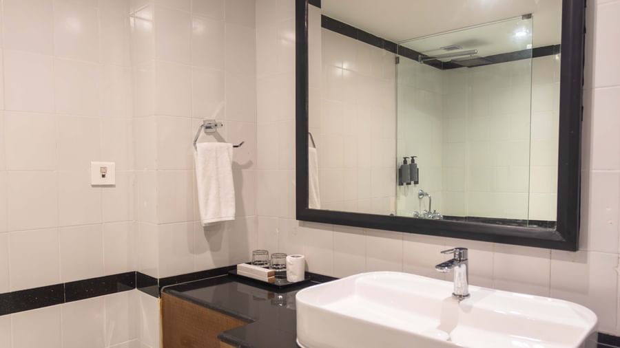 A contemporary bathroom at Shilton International, Kochi, with a large mirror, vessel sink, and modern toilet.