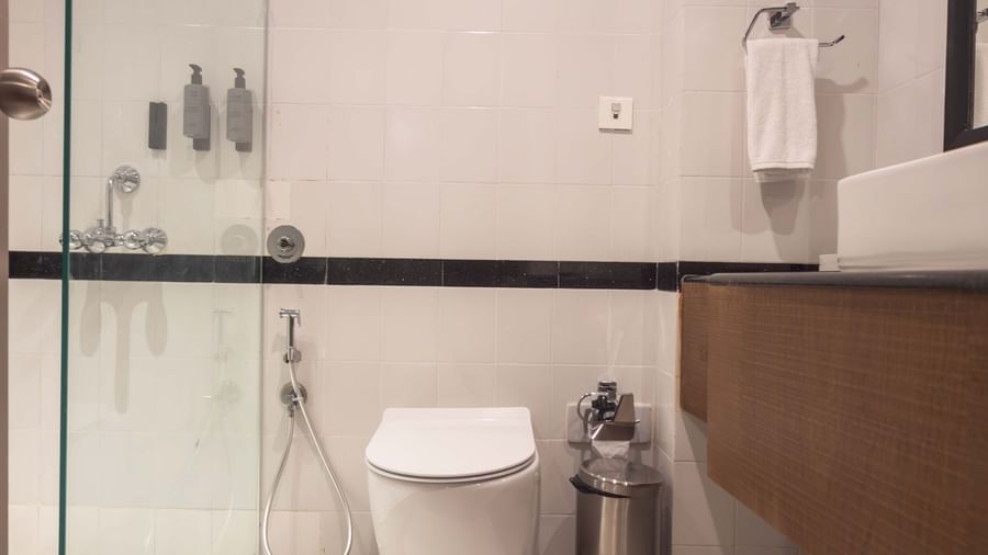  A spacious bathroom at Shilton International, Kochi, featuring a modern toilet, sleek vanity, and a shower enclosure.