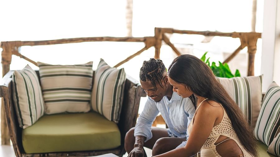 A man and a woman sitting in a lounge area with palm trees in the background - Shooting Star Boutique Hotel.