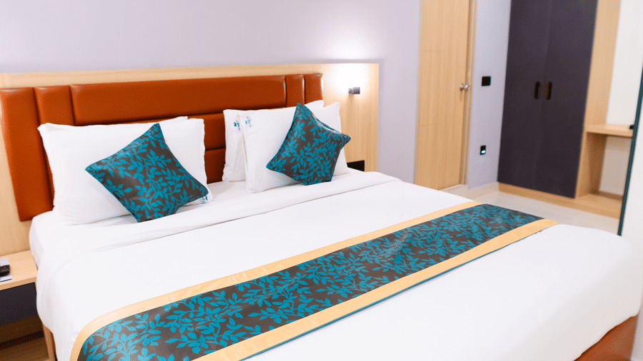 Close-up view of a neatly made bed with 2 pairs of pillows and a duvet placed neatly at Sunrise Business Hotel, Hyderabad.