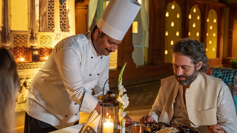 A chef serving two guests seated in a dining area at Surpura Bagh.