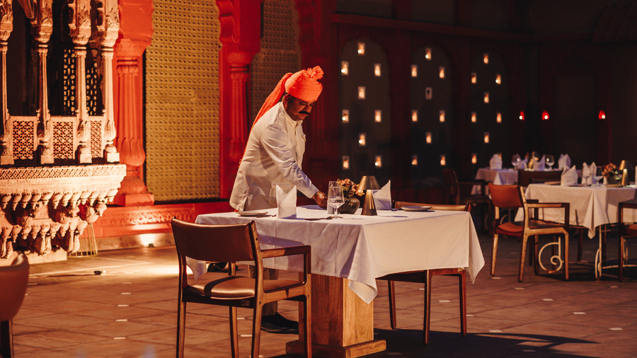 An outdoor dining setup with a traditionally dressed server at Surpura Bagh.