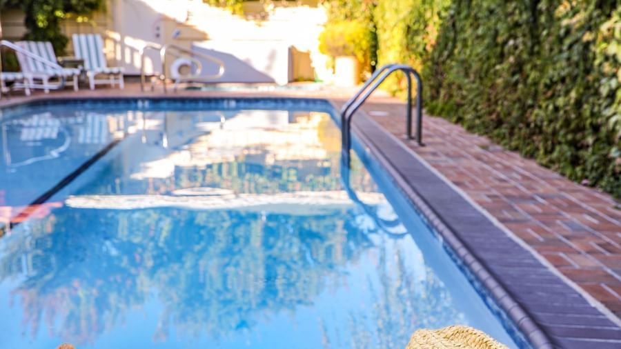 A first-person view of legs by the Tallman Hotel pool, showcasing a hat and sunglasses on a towel.