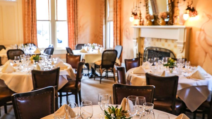 A well-lit dining area of Tallman Hotel arranged in a cluster formation and tables neatly draped with cloth and cutlery.