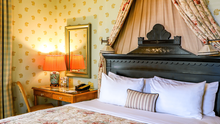A view of the Veranda Room featuring floral linens on the double bed, a bedside table, a wall-mounted mirror and a rustic bedroom setting