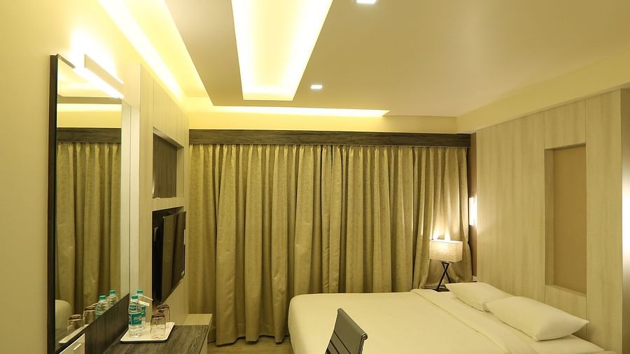 Premium Room shown with a king size bed, desk, chair, and mirror, illuminated by warm lighting - TGI SPS Grand, Coimbatore