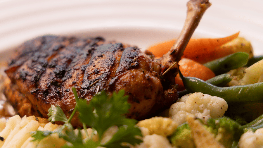 A close-up shot of a grilled chicken dish served with creamy mashed potatoes and sauteed vegetables.