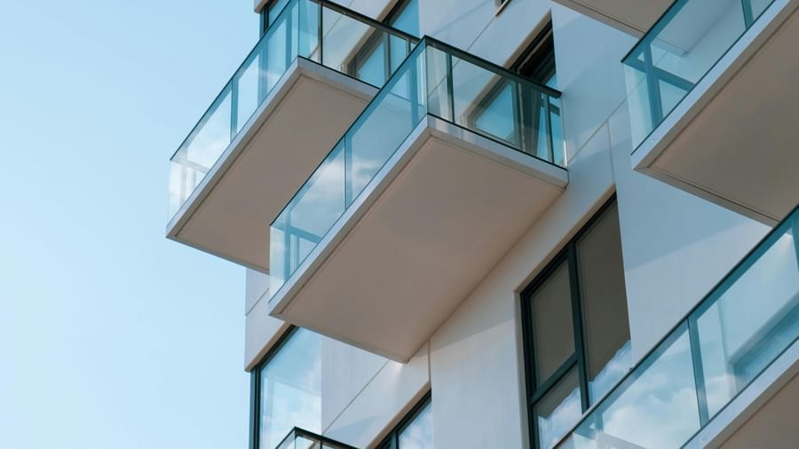 Modern apartment building facade with multiple balconies and glass railings against a clear blue sky.