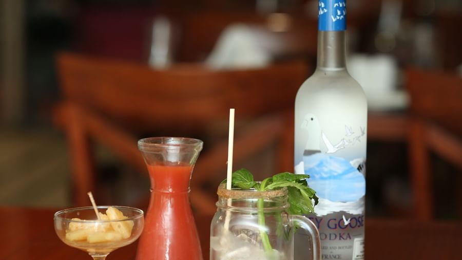 A selection of bottled drinks and a garnished glass in a wooden holder at The Citi Residenci Hotel, Durgapur.