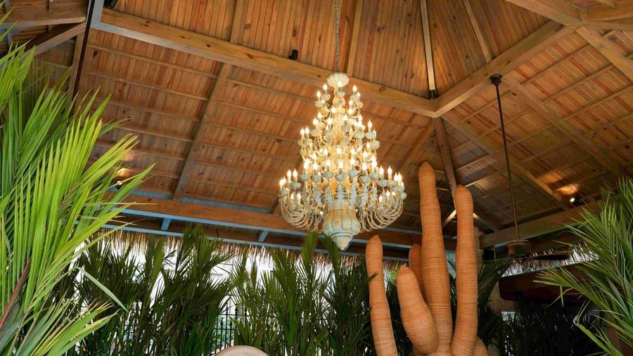 A chandelier hanging from the thatched roof with white and beige coloured chequered tiles in the foreground, surrounded by lush tropical greenery at The Evren, Vagator.