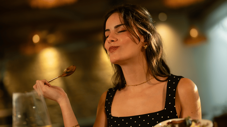 A woman seated at a bar counter holding a plate of food, a candle, and warm lighting visible at The Evren, Vagator