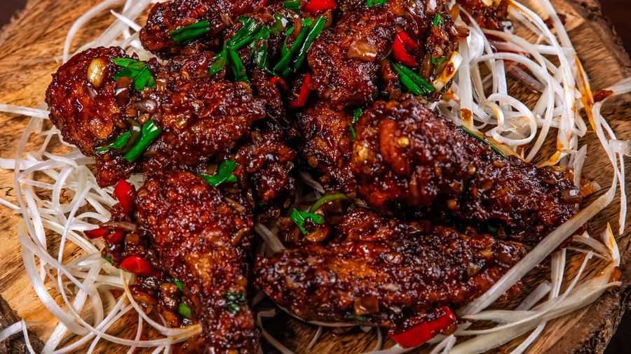 A bowl of crispy, saucy fried chicken strips garnished with sesame seeds and spring onions, placed on shredded white cabbage on a rustic wooden base at The Hamuse Hotel, Kodaikanal.