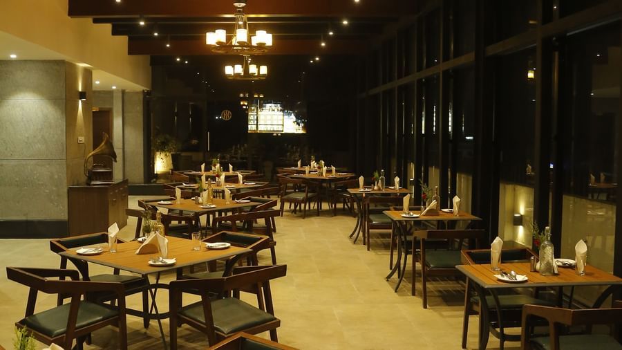 A rooftop dining area under night sky with variously arranged seating at The Hamuse Hotel, Kodaikanal.