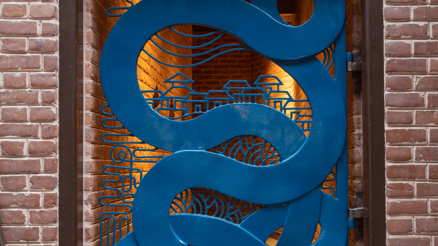 An ornate, vibrant blue metal security gate with abstract fluid cutouts set into a traditional red brick entryway in Bhaktapur, Nepal.