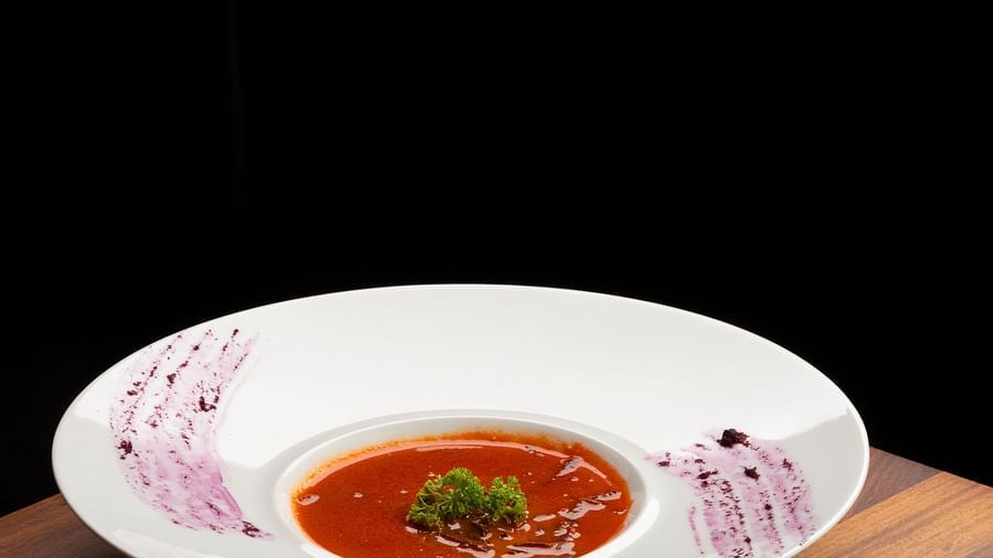 A bowl of soup with bread on a side plate, placed on a wooden table with a spoon at The Qualia Resort Club & Brewery, Udaipur.