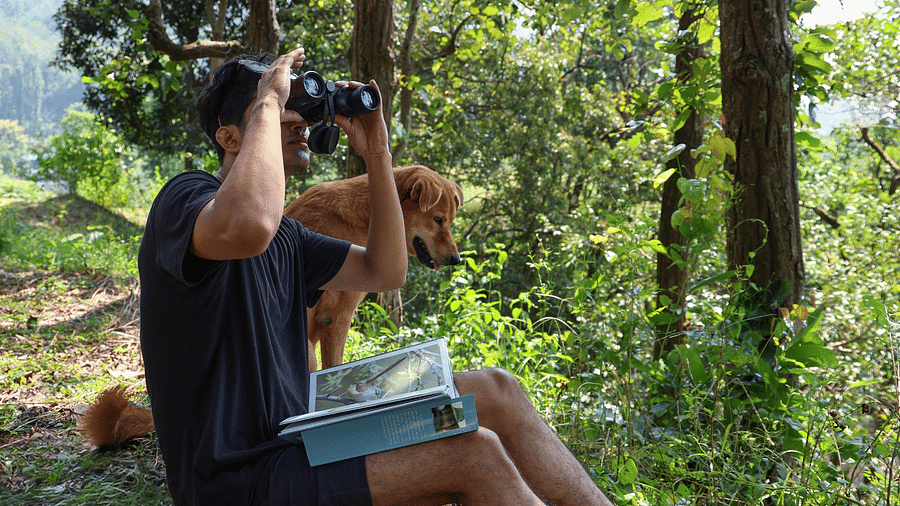 A man sitting on a cliff watching through binoculars at The Sylvan Retreat, Dehradun.