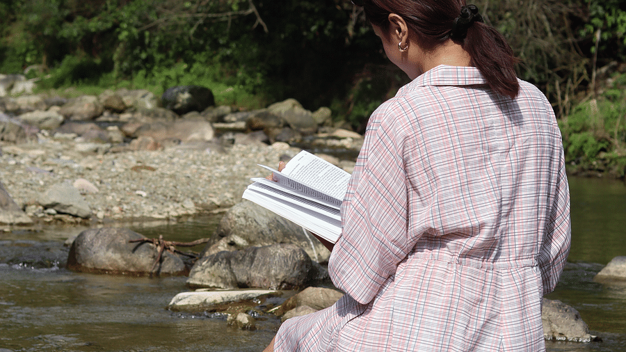 A woman reading a book sitting by the stream at A man flying a kite at The Sylvan Retreat, Dehradun.