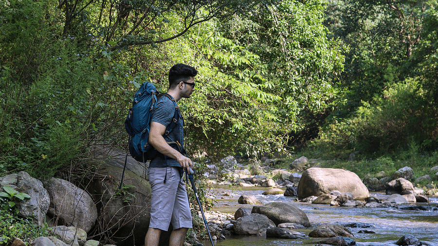 A man standing on a rock next to a water stream at the Sylvan Retreat, Dehradun.