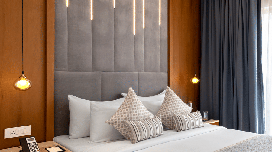 A sophisticated hotel bedroom interior showcasing a king size bed set against an illuminated wooden headboard panel at Tiara by MPS.