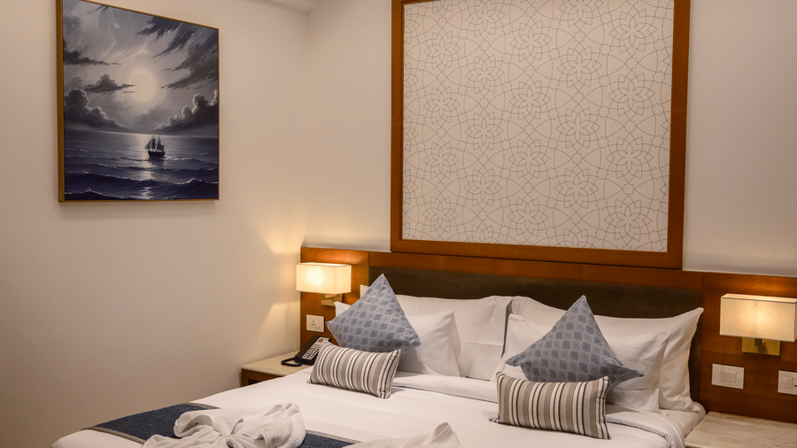 A cosy bedroom layout showing a king size bed decorated with folded towels, a wall painting, and a bedside lamp at Tiara by MPS.