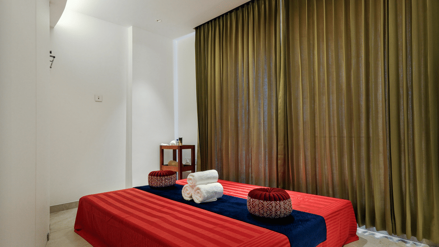A low spa bed covered in a bright sheet is arranged on the floor of a treatment room with long curtains and a recessed ceiling at Tiara by MPS.