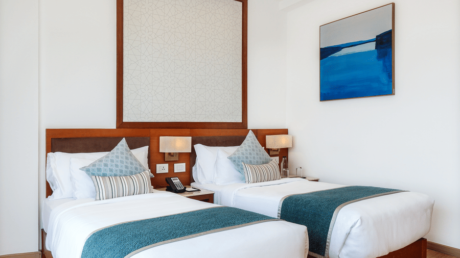 A well-lit hotel room arranged with 2 single beds, a wall painting, and a warm recessed ceiling border at Tiara by MPS.
