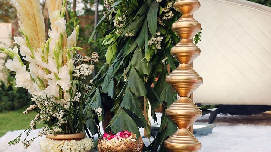 Tall brass lamp and large brass pots placed beside a bamboo and floral decor at Tisya Farms, Gurgaon.