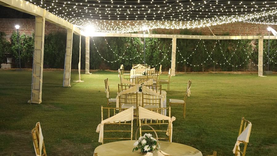 Close-up of a banquet table and chairs under decorative lights on the lawn at Tisya Farms, Gurgaon.