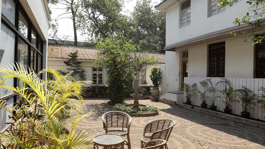 A circular stone courtyard at Trance Sunderban Resort featuring woven chairs, small tables, and potted palms outside the buildings.