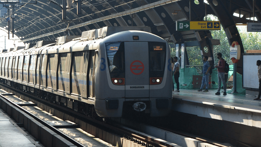 A vertical view of an urban metro train pulling into an elevated station platform with a curved metal roof structure.