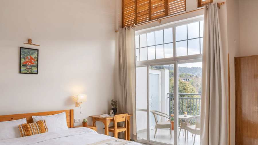 A cropped image of a Ziran Retreat bedroom with a bed, bedside table, and a large window with white curtains, showing a partial view of the room and the window.